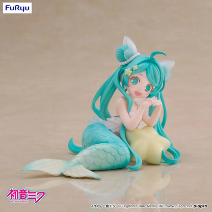 Pastel mermaid Hatsune Miku desktop fairy figure lounging on a star cushion with a mint-green tail and twin-tails, displayed on a desk with seashells and a keyboard in the background.