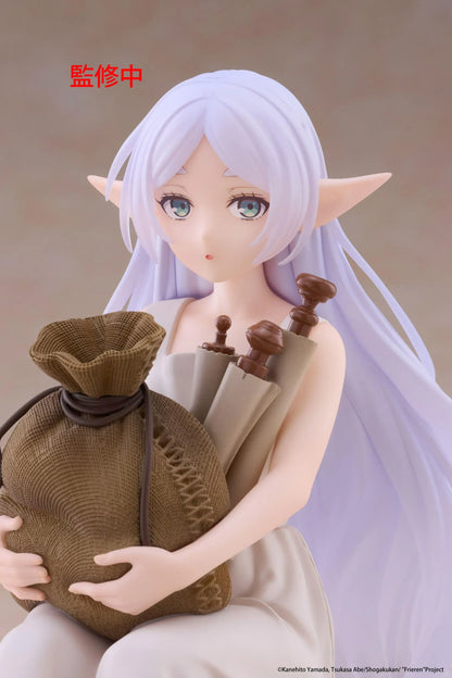 Desktop Cute Frieren In Training Ver. figure seated on a gray stone block, wearing a cream dress and brown sandals while holding a sack beside rolled scrolls.