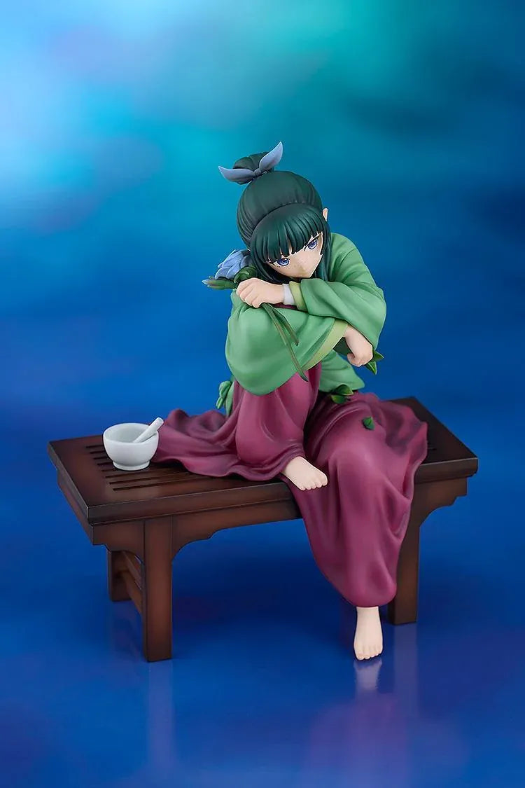 Maomao 1/7 scale figure seated barefoot on a wooden bench, wearing a green top and plum skirt, holding a blue flower beside a mortar and pestle.