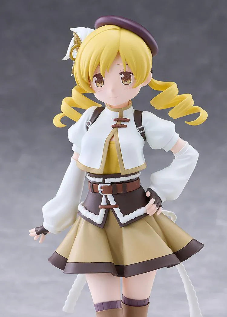 Mami Tomoe figure with blonde spiral curls, a brown hat, white and gold outfit, and tall brown boots, posing with one hand on her hip.