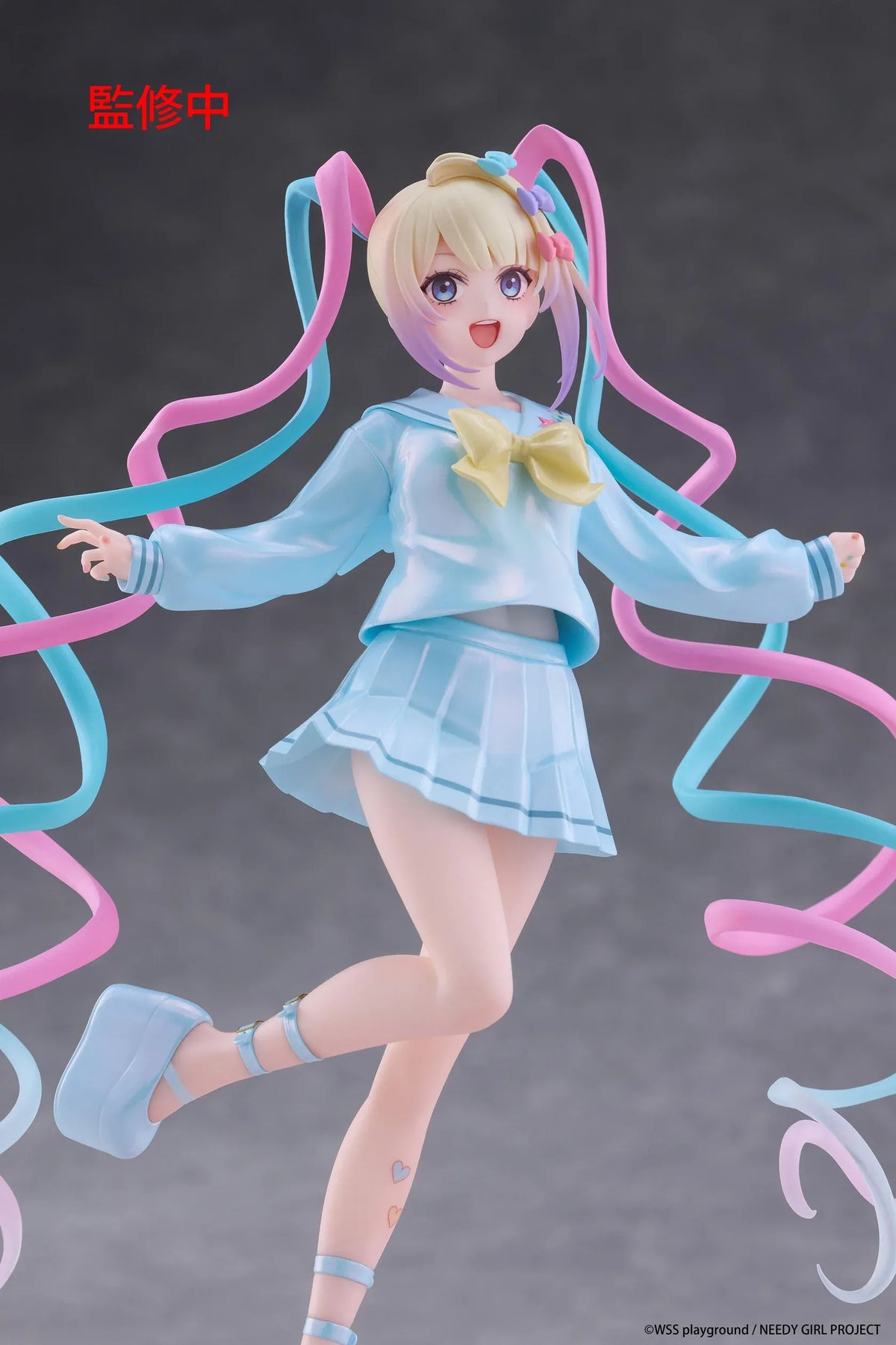 Needy Girl Overdose OMGKawaiiAngel Coreful Figure featuring a blonde-haired anime girl with blue eyes, long pink and blue twin-tails, a pastel-blue sailor-style outfit, yellow bow, and matching shoes posed on a pink heart-shaped base.