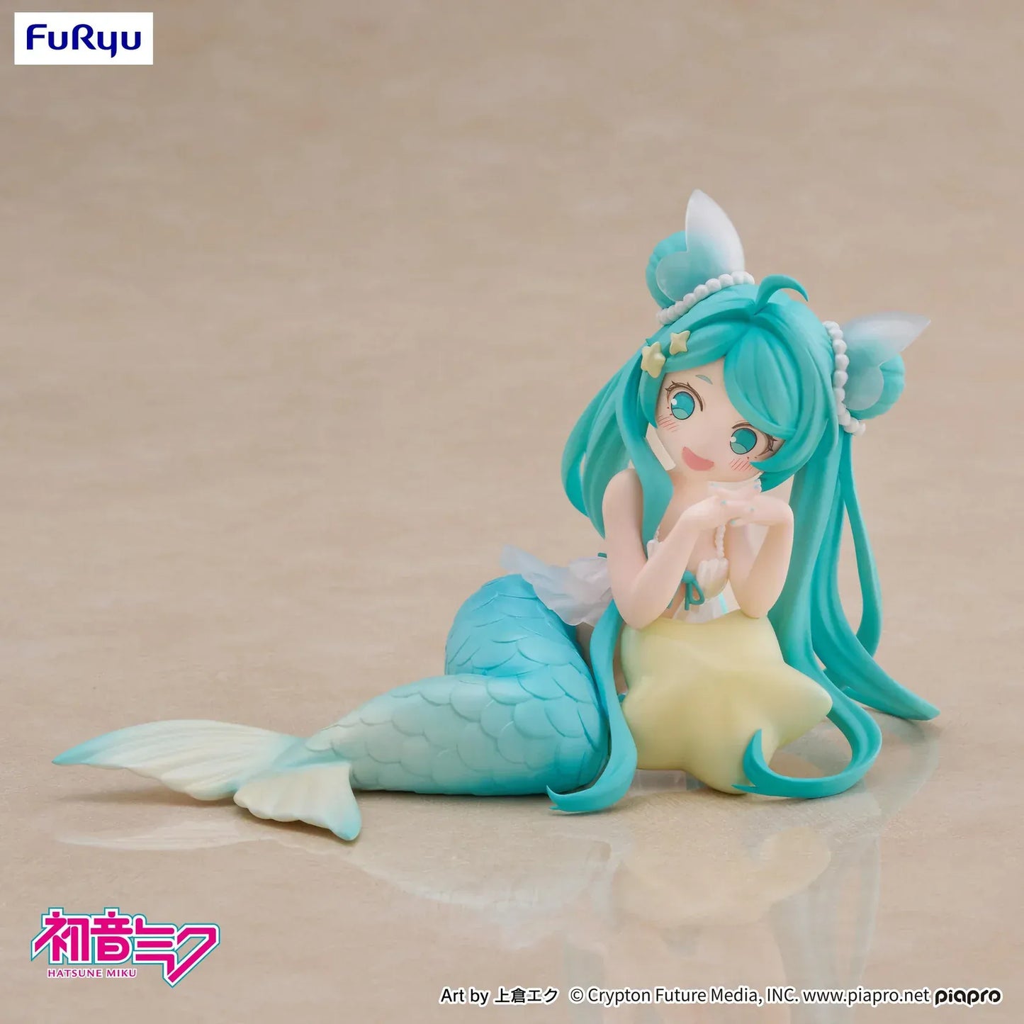 Pastel mermaid Hatsune Miku desktop fairy figure lounging on a star cushion with a mint-green tail and twin-tails, displayed on a desk with seashells and a keyboard in the background.