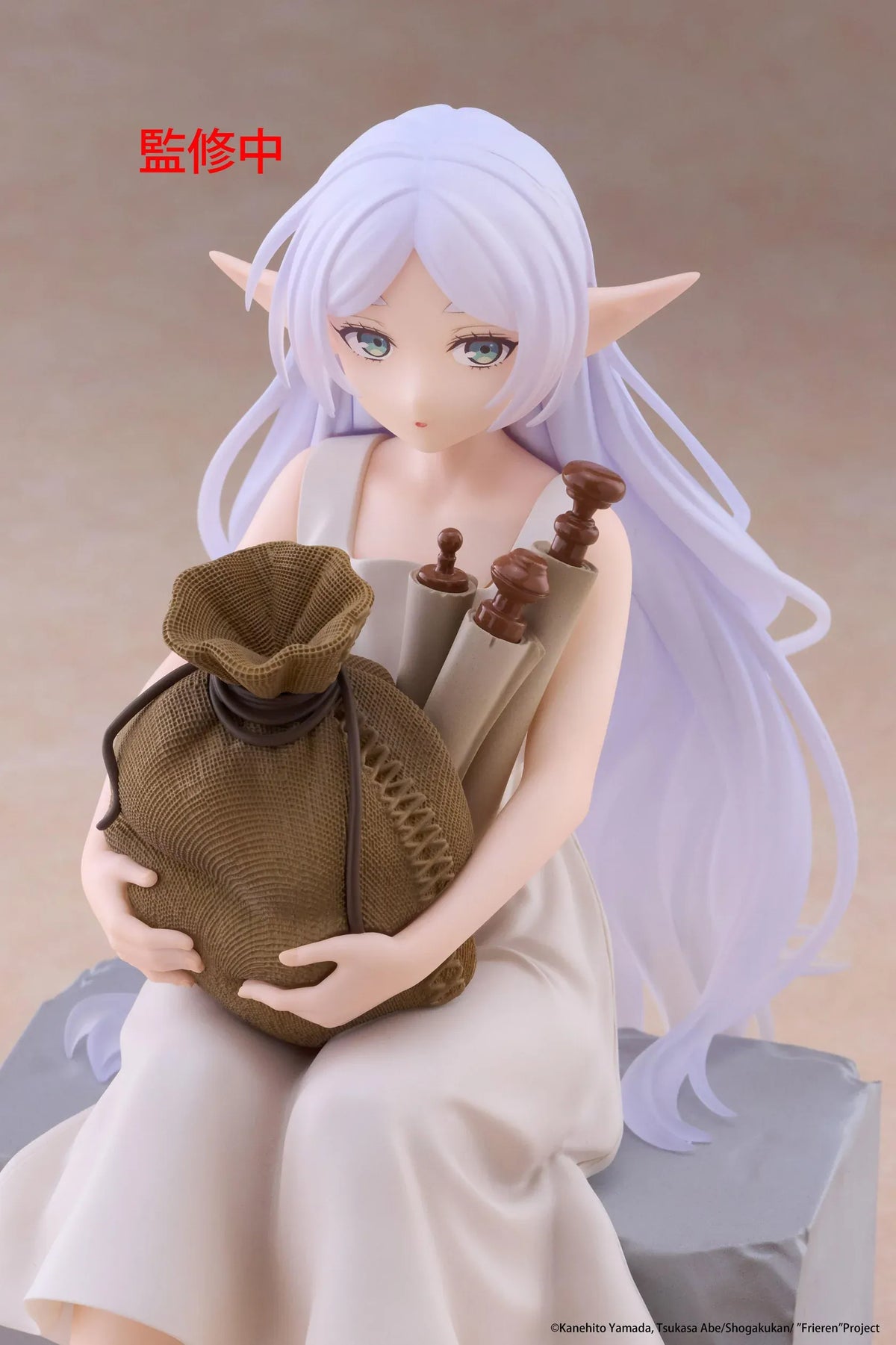Desktop Cute Frieren In Training Ver. figure seated on a gray stone block, wearing a cream dress and brown sandals while holding a sack beside rolled scrolls.