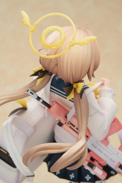 Blue Archive Hifumi figure smiling with one foot lifted, wearing a white cardigan and navy skirt, carrying a bird-themed bag and rifle on a yellow base.