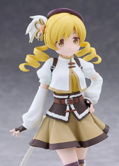 Mami Tomoe figure with blonde spiral curls, a brown hat, white and gold outfit, and tall brown boots, posing with one hand on her hip.