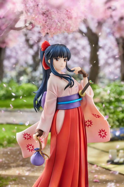 Sakura Wars Sakura Shinguji 1/7 Scale Figure featuring a dark blue-haired anime girl with brown eyes, a red hair ribbon, pink kimono-style top, purple obi, flowing red hakama skirt, sword accessory, and purple pouch on a transparent circular base.