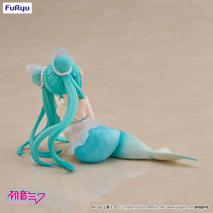 Pastel mermaid Hatsune Miku desktop fairy figure lounging on a star cushion with a mint-green tail and twin-tails, displayed on a desk with seashells and a keyboard in the background.