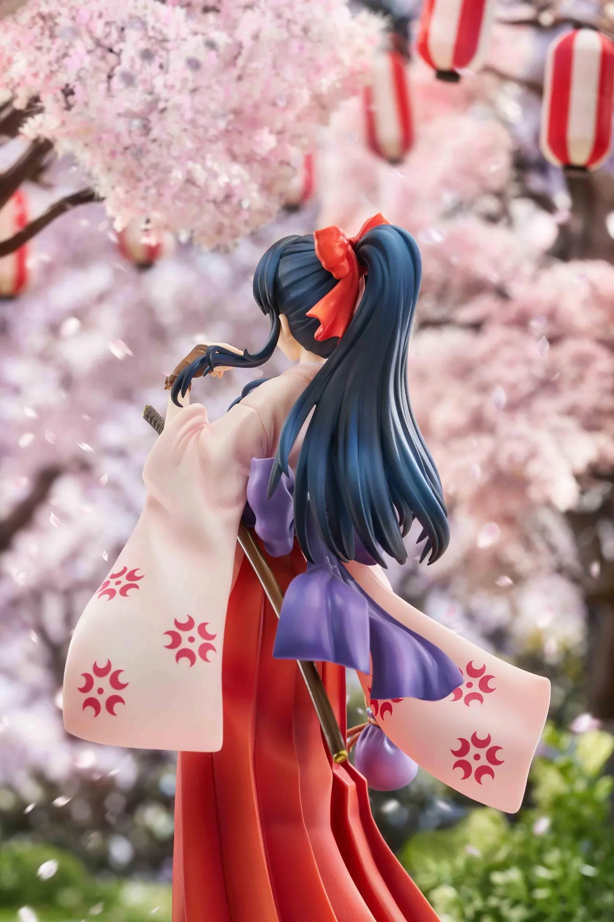 Sakura Wars Sakura Shinguji 1/7 Scale Figure featuring a dark blue-haired anime girl with brown eyes, a red hair ribbon, pink kimono-style top, purple obi, flowing red hakama skirt, sword accessory, and purple pouch on a transparent circular base.