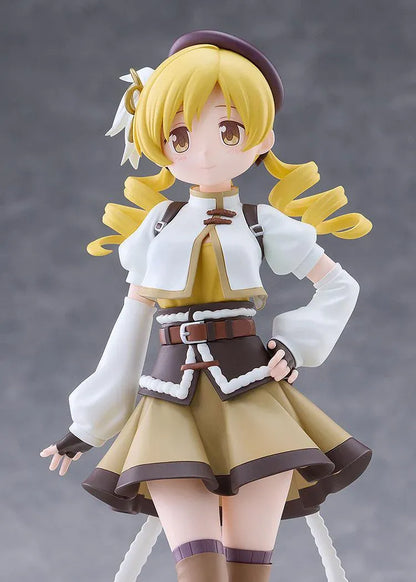 Mami Tomoe figure with blonde spiral curls, a brown hat, white and gold outfit, and tall brown boots, posing with one hand on her hip.