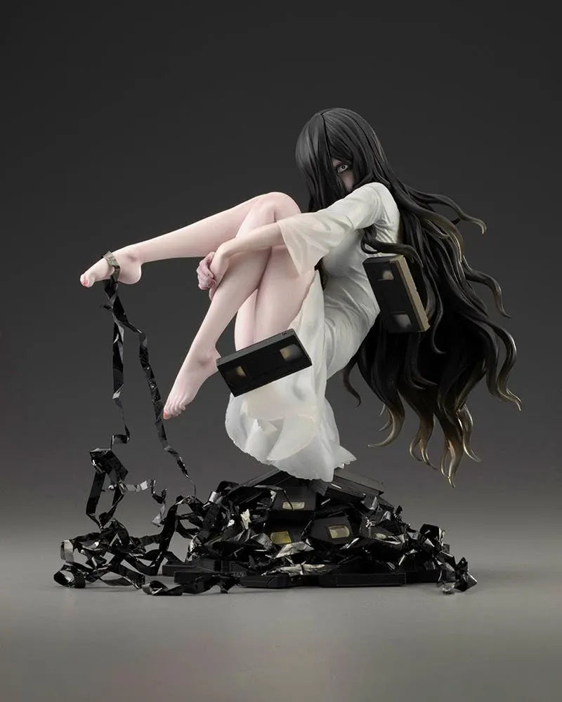 Sadako BISHOUJO Sadako 1/7 Scale Figure (Rerelease) featuring a long black-haired horror character wearing a flowing white dress, seated above a pile of VHS tapes with tangled black film ribbons.