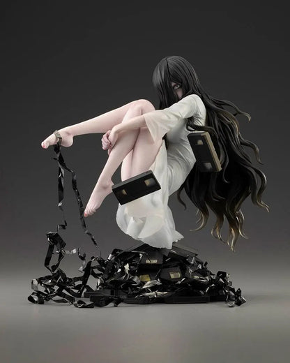Sadako BISHOUJO Sadako 1/7 Scale Figure (Rerelease) featuring a long black-haired horror character wearing a flowing white dress, seated above a pile of VHS tapes with tangled black film ribbons.