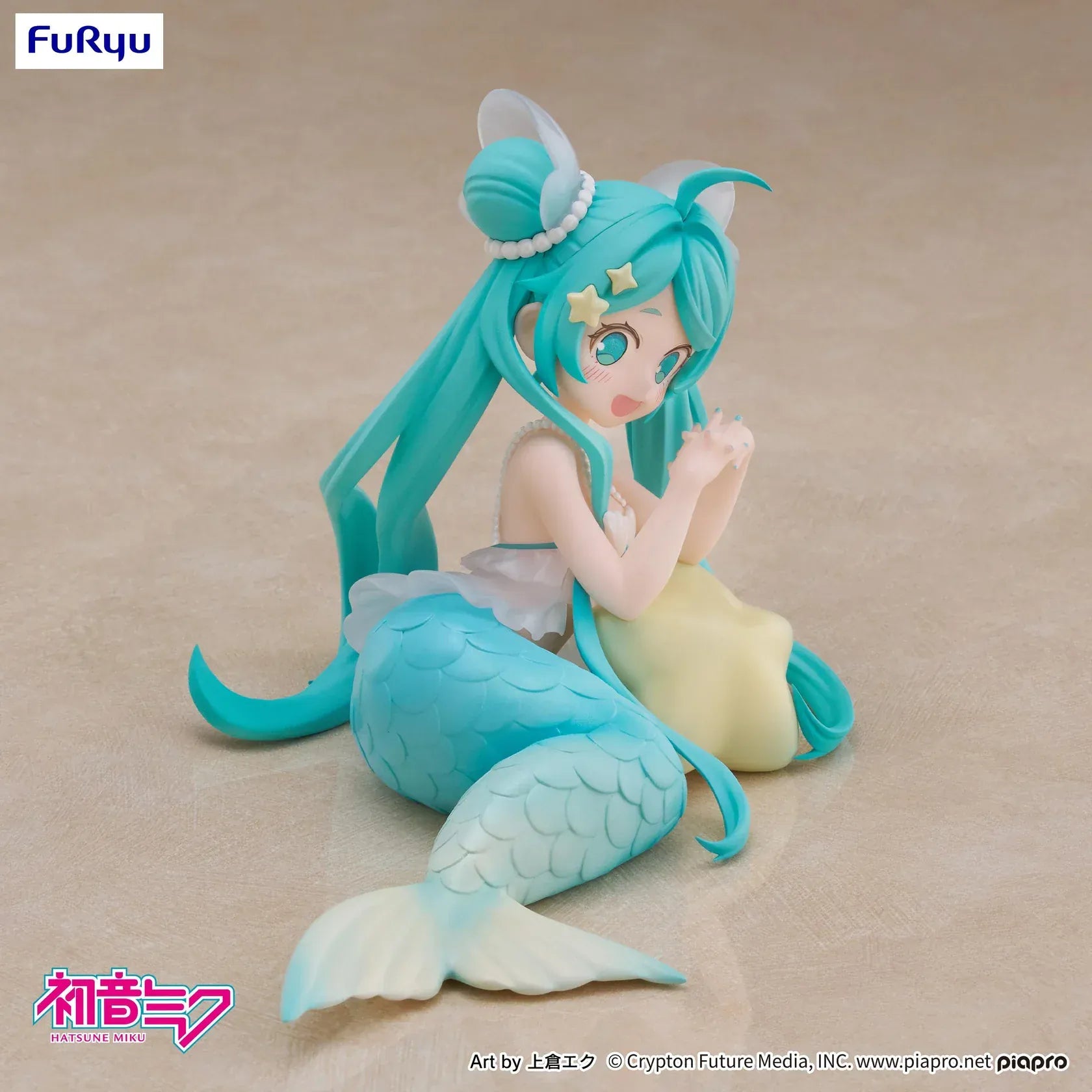 Pastel mermaid Hatsune Miku desktop fairy figure lounging on a star cushion with a mint-green tail and twin-tails, displayed on a desk with seashells and a keyboard in the background.