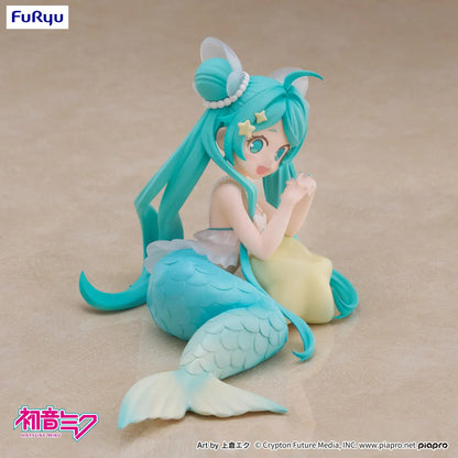 Pastel mermaid Hatsune Miku desktop fairy figure lounging on a star cushion with a mint-green tail and twin-tails, displayed on a desk with seashells and a keyboard in the background.