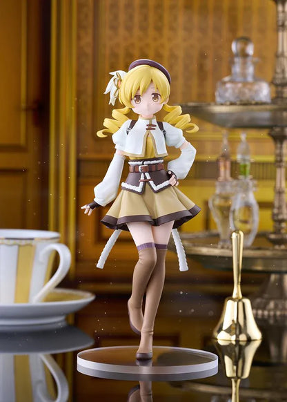 Mami Tomoe figure with blonde spiral curls, a brown hat, white and gold outfit, and tall brown boots, posing with one hand on her hip.