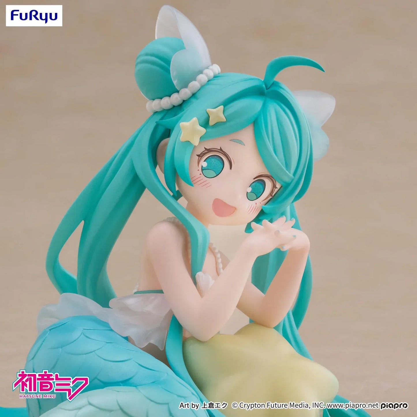 Pastel mermaid Hatsune Miku desktop fairy figure lounging on a star cushion with a mint-green tail and twin-tails, displayed on a desk with seashells and a keyboard in the background.