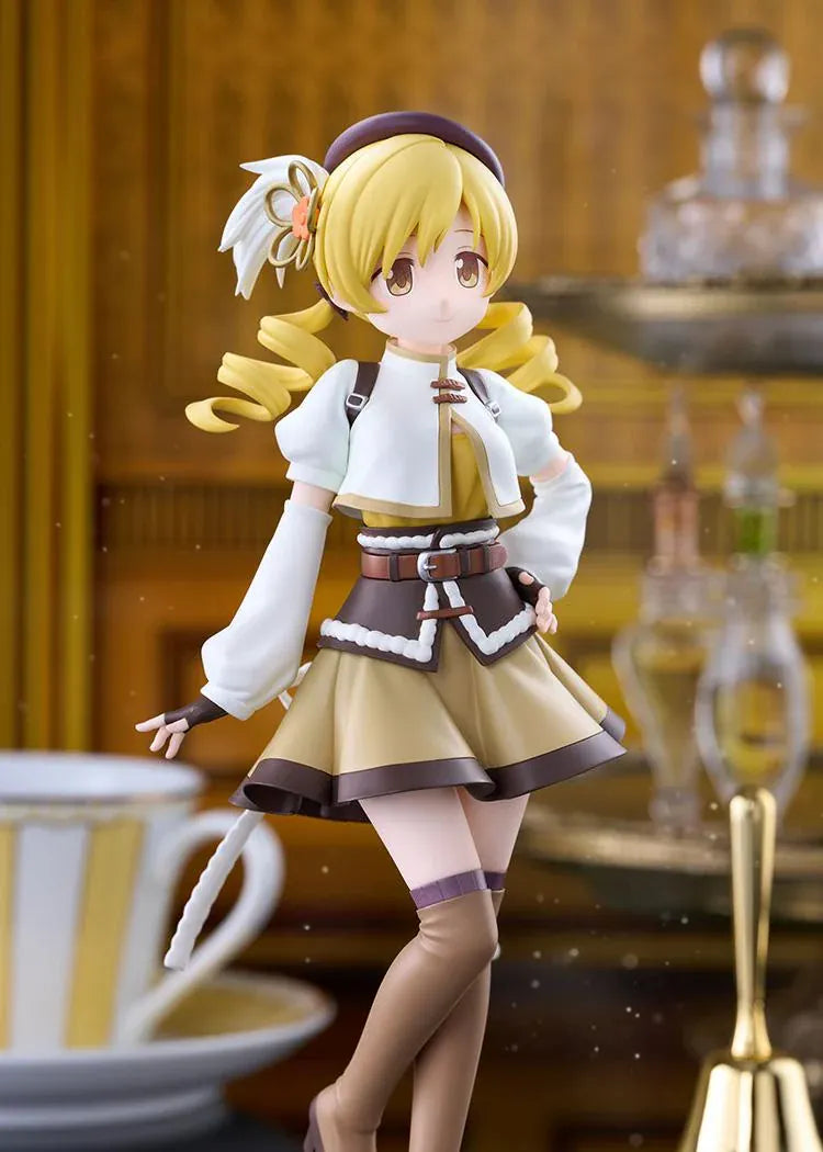 Mami Tomoe figure with blonde spiral curls, a brown hat, white and gold outfit, and tall brown boots, posing with one hand on her hip.