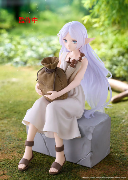 Desktop Cute Frieren In Training Ver. figure seated on a gray stone block, wearing a cream dress and brown sandals while holding a sack beside rolled scrolls.