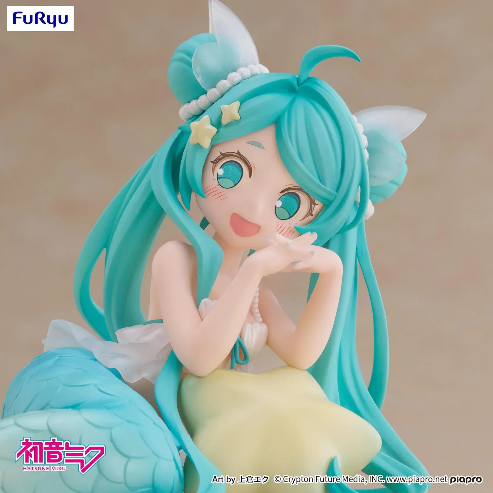 Pastel mermaid Hatsune Miku desktop fairy figure lounging on a star cushion with a mint-green tail and twin-tails, displayed on a desk with seashells and a keyboard in the background.