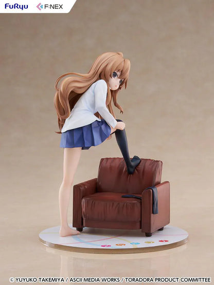 1/7 scale Toradora figure of Taiga Aisaka at home, barefoot and leaning on a leather armchair while pulling on a black thigh-high sock, wearing her school shirt and blue skirt.