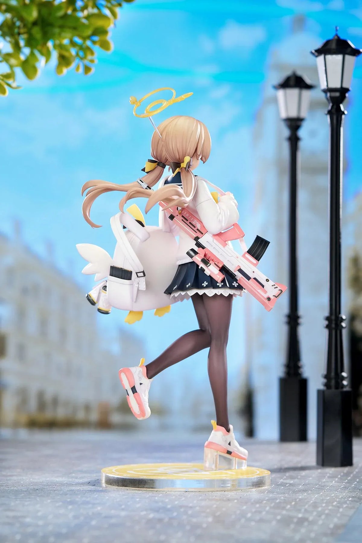 Blue Archive Hifumi figure smiling with one foot lifted, wearing a white cardigan and navy skirt, carrying a bird-themed bag and rifle on a yellow base.