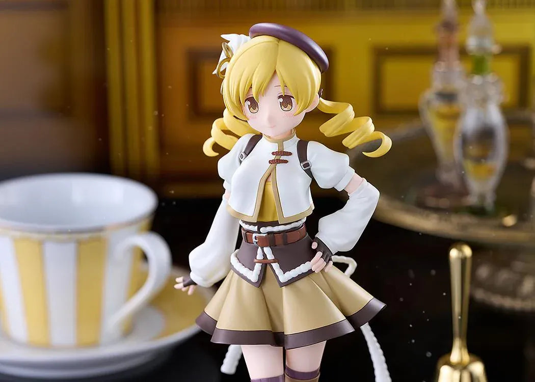 Mami Tomoe figure with blonde spiral curls, a brown hat, white and gold outfit, and tall brown boots, posing with one hand on her hip.