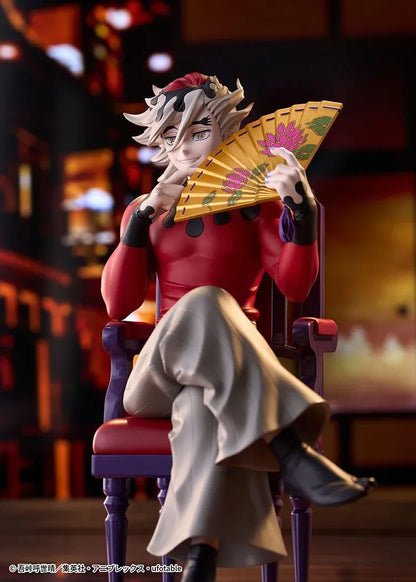 Doma figure seated cross-legged on a purple chair with red cushions, holding a gold floral fan and wearing a red top with gray trousers.