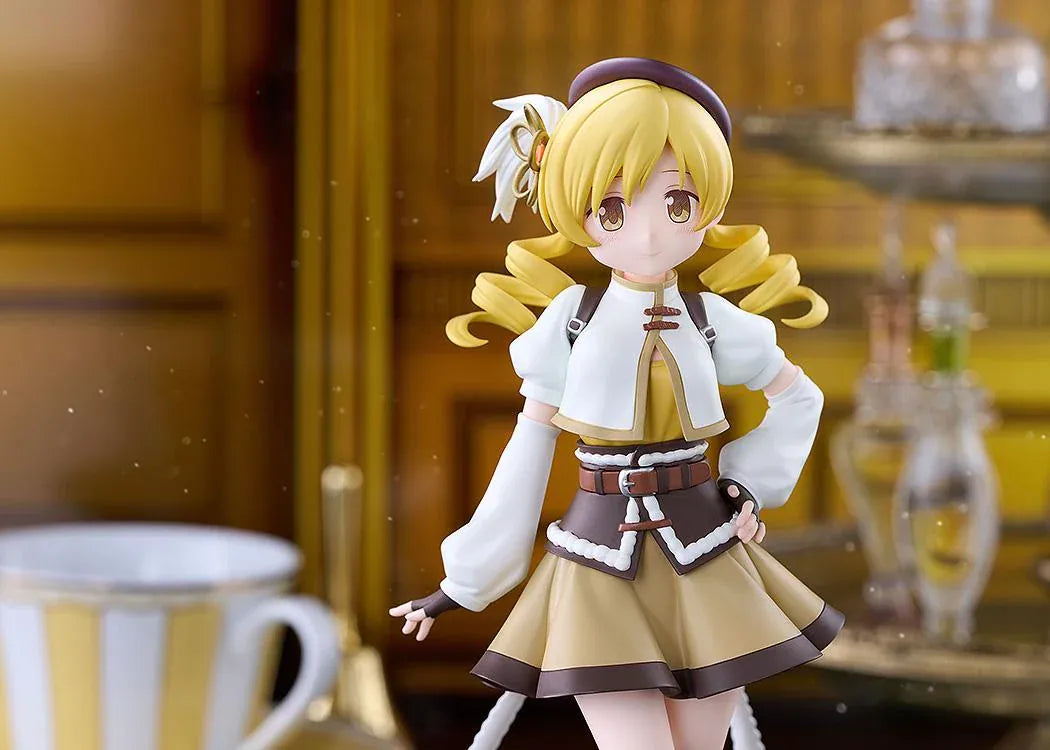 Mami Tomoe figure with blonde spiral curls, a brown hat, white and gold outfit, and tall brown boots, posing with one hand on her hip.