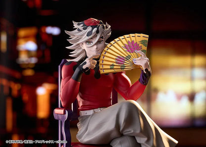 Doma figure seated cross-legged on a purple chair with red cushions, holding a gold floral fan and wearing a red top with gray trousers.