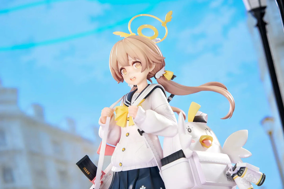 Blue Archive Hifumi figure smiling with one foot lifted, wearing a white cardigan and navy skirt, carrying a bird-themed bag and rifle on a yellow base.