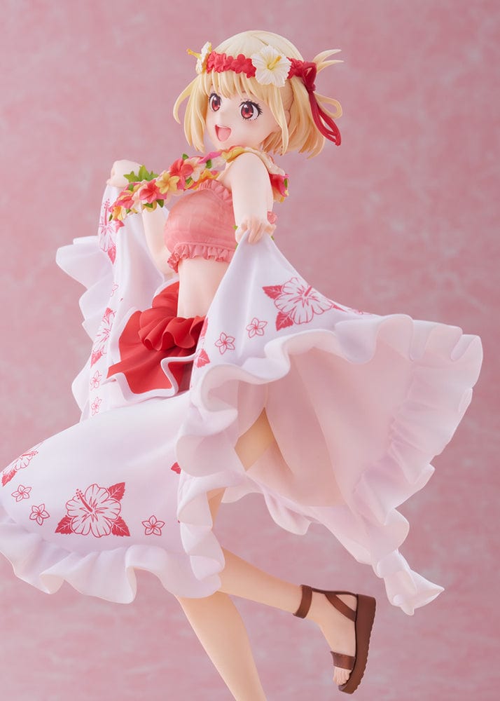 A 1/7 scale figure of Chisato Nishikigi from "Lycoris Recoil," depicted in a Hawaiian version outfit. She has a cheerful expression, blonde hair with flower adornments, and is holding a floral lei. The figure wears a white skirt with pink hibiscus prints and a ruffled red top, poised mid-twirl on a sandy base resembling a beach.
