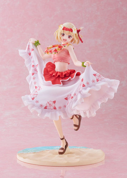 A 1/7 scale figure of Chisato Nishikigi from "Lycoris Recoil," depicted in a Hawaiian version outfit. She has a cheerful expression, blonde hair with flower adornments, and is holding a floral lei. The figure wears a white skirt with pink hibiscus prints and a ruffled red top, poised mid-twirl on a sandy base resembling a beach.