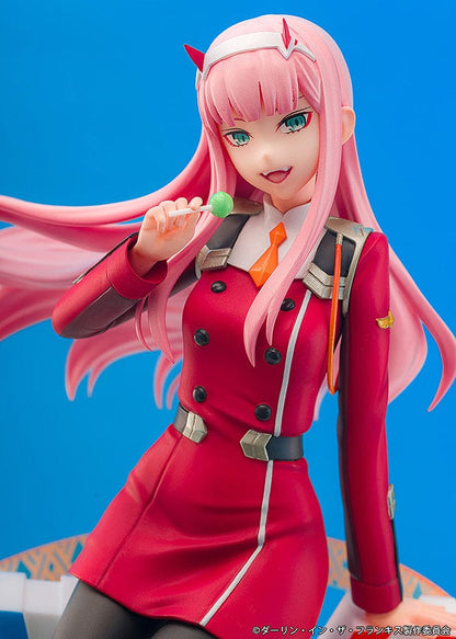 Darling in the Franxx Zero Two 1/7 Scale Figure in red outfit, sitting on a geometric base with "002" emblem, holding a lollipop with a mischievous expression.