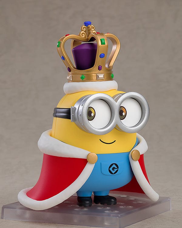 A Nendoroid figure of Bob, the beloved character from the Minions, in his characteristic yellow and blue attire. He's shown with a joyous expression, wearing his typical silver goggles, and accompanied by a teddy bear. In some poses, Bob is waving enthusiastically, while in others, he dons a king's crown and a cape, or holds a bedtime teddy bear, showcasing his playful and lovable personality.