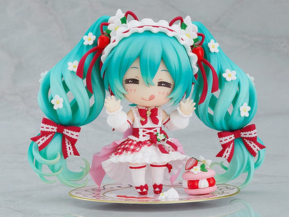 “Nendoroid No.1939 Hatsune Miku (15th Anniversary Ver.) re-run—teal twin-tails with daisies and red bows, frilly dress, holding a strawberry and gold fork, macaron on plate base.”

