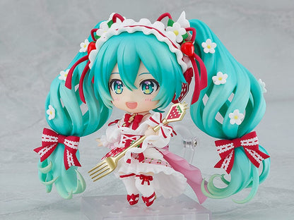 “Nendoroid No.1939 Hatsune Miku (15th Anniversary Ver.) re-run—teal twin-tails with daisies and red bows, frilly dress, holding a strawberry and gold fork, macaron on plate base.”

