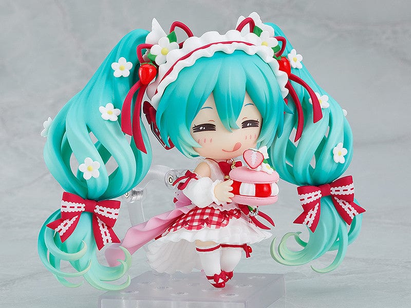 “Nendoroid No.1939 Hatsune Miku (15th Anniversary Ver.) re-run—teal twin-tails with daisies and red bows, frilly dress, holding a strawberry and gold fork, macaron on plate base.”

