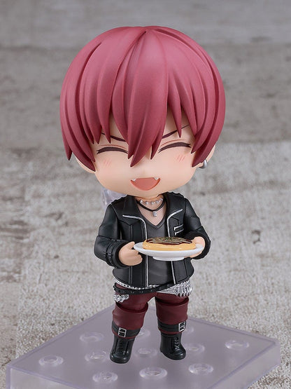 IDOLiSH7 Nendoroid Toma Inumaru figure featuring a black jacket, burgundy pants, and confident pose with interchangeable faceplates, set against a textured gray background.