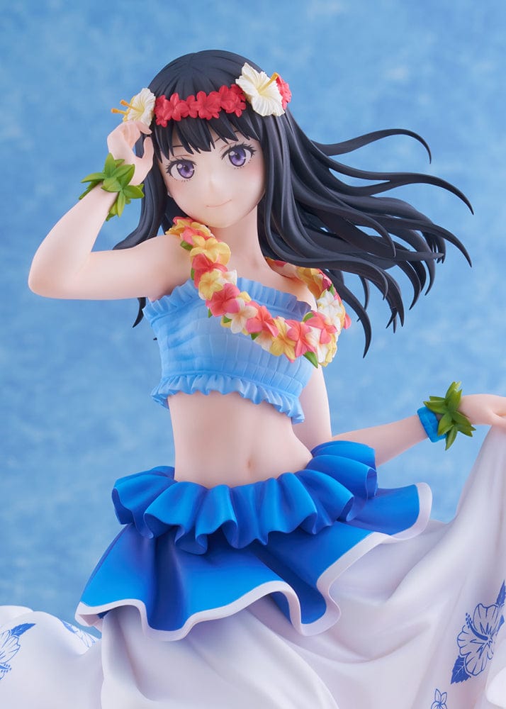 A 1/7 scale figure of Takina Inoue from "Lycoris Recoil" in a Hawaiian version ensemble, with long black hair and a peaceful expression. She is adorned with a floral lei and hairpiece, wearing a blue ruffled top and a white skirt with blue floral prints. The dynamic pose captures her mid-dance, with her skirt lifted to reveal a layered blue underskirt, standing on a sandy beach base with a hint of ocean wave.
