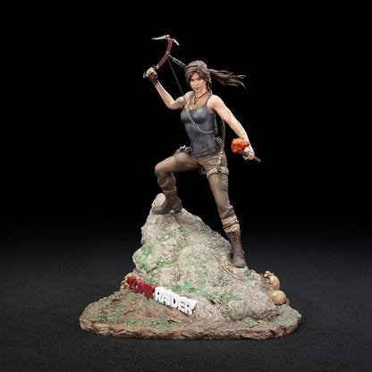 Tomb Raider Lara Croft (Survivor Era) Statue holding climbing axe and torch, in rugged survival gear on rocky base with foliage and skull