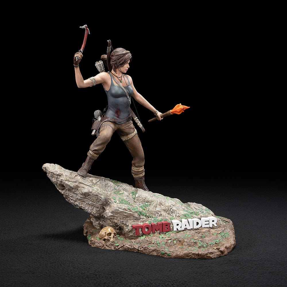 Tomb Raider Lara Croft (Survivor Era) Statue holding climbing axe and torch, in rugged survival gear on rocky base with foliage and skull