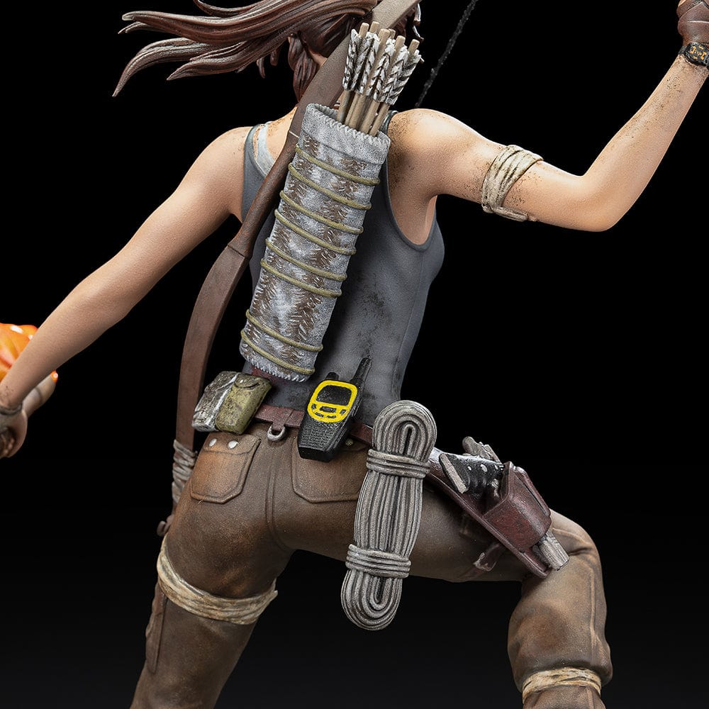 Tomb Raider Lara Croft (Survivor Era) Statue holding climbing axe and torch, in rugged survival gear on rocky base with foliage and skull