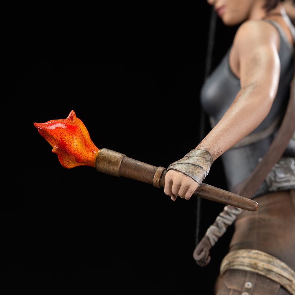 Tomb Raider Lara Croft (Survivor Era) Statue holding climbing axe and torch, in rugged survival gear on rocky base with foliage and skull