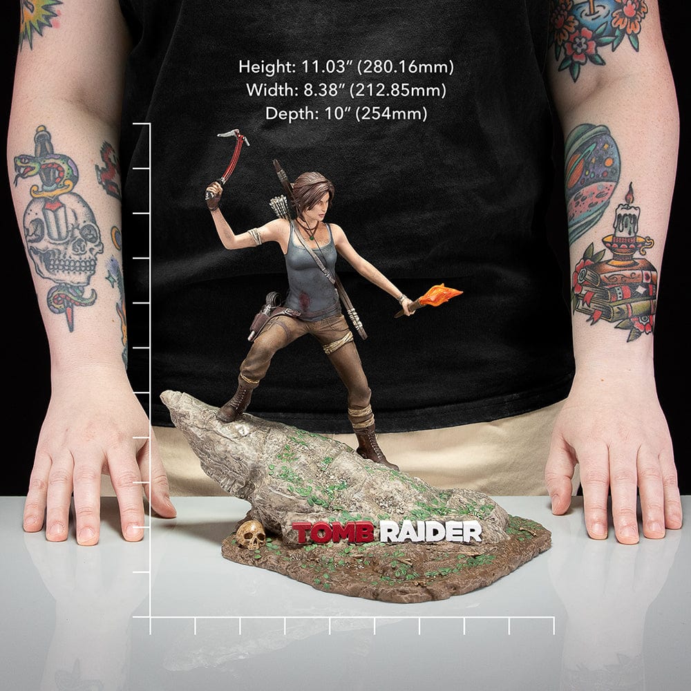 Tomb Raider Lara Croft (Survivor Era) Statue holding climbing axe and torch, in rugged survival gear on rocky base with foliage and skull