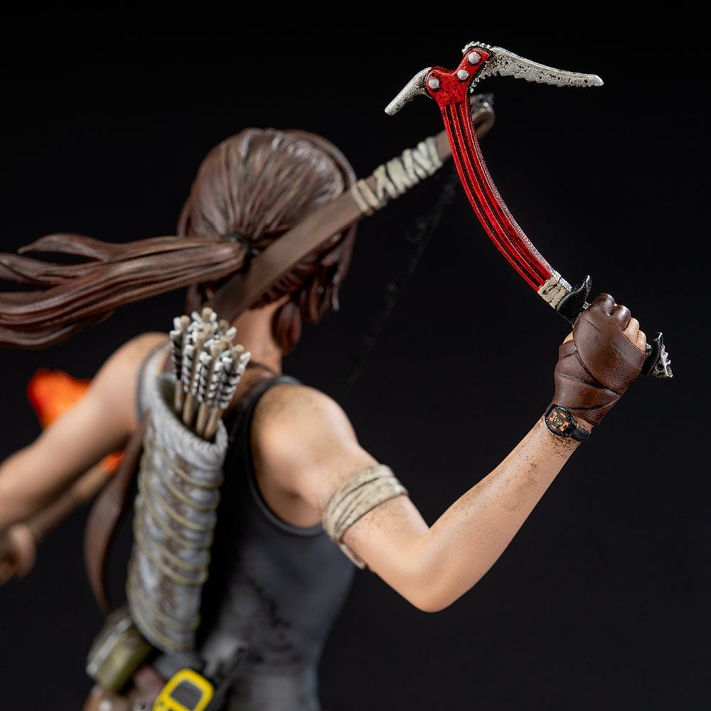 Tomb Raider Lara Croft (Survivor Era) Statue holding climbing axe and torch, in rugged survival gear on rocky base with foliage and skull