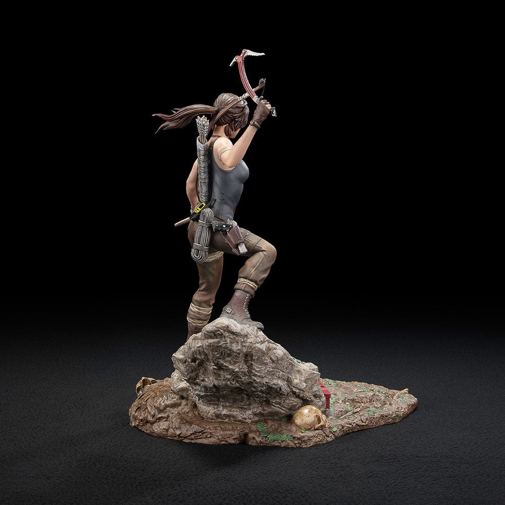 Tomb Raider Lara Croft (Survivor Era) Statue holding climbing axe and torch, in rugged survival gear on rocky base with foliage and skull